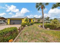 Bright yellow home featuring a metal roof, rock accents, lush landscaping, and an attached two-car garage at 1173 Brown St, Englewood, FL 34224