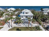 Beautiful two-story beach house featuring a white exterior, staircase, and a meticulously landscaped yard with palm trees at 9 Peekins Cove Dr, Boca Grande, FL 33921