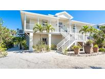 Two-story home with dual staircases and white exterior, accented by tropical landscaping and bright blue sky at 62 Tarpon Way, Placida, FL 33946