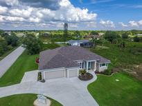 Expansive aerial view of a modern home with a three-car garage, lush lawn, and a winding driveway at 13252 Keystone Blvd, Port Charlotte, FL 33981