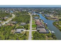 Wide aerial shot of a gray-roofed single-Gathering home surrounded by verdant trees, canals, and neighboring houses at 15613 Alsask Cir, Port Charlotte, FL 33981