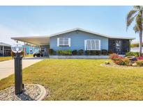 Inviting single-story mobile home with a carport, lush lawn and flourishing tropical flowers at 816 Tangerine Woods Blvd, Englewood, FL 34223