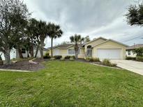Charming yellow home featuring a well-manicured lawn and decorative palm trees in the front yard at 67 Marker Rd, Rotonda West, FL 33947
