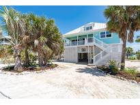 Charming stilt home with white railing, stairs, and tropical landscaping at 180 S Gulf Blvd, Placida, FL 33946