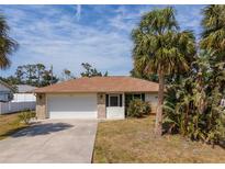 Charming single-story home featuring a two-car garage, manicured lawn, and tropical landscaping at 3189 Siesta Dr, Venice, FL 34293