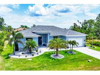 Charming light blue home featuring a gray roof and manicured lawn with decorative palm trees at 13348 Boabadilla Ln, Port Charlotte, FL 33981