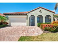 Inviting home with a red tile roof, arched entry, and lush landscaping along a brick driveway and a two car garage at 23590 Copperleaf Dr, Venice, FL 34293