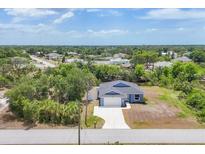 Aerial view of a charming blue single-Gathering home with an attached garage, lush landscaping, and a long driveway at 7332 Brandywine Dr, Englewood, FL 34224