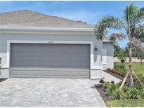 Modern home featuring a gray garage door, a brick driveway, and well-manicured landscaping at 8673 Seasalt Loop, Englewood, FL 34224