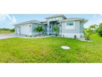 Well-maintained single-Gathering home features a two-car garage and a lush green lawn and tropical landscaping at 13344 Gershwin Ln, Port Charlotte, FL 33981