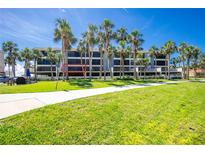 Three-story condo building with palm trees, balconies, and manicured lawn in a sunny, tropical setting at 1551 Beach Rd # 212, Englewood, FL 34223