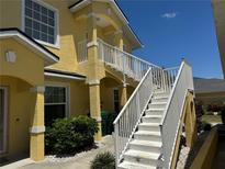 Two-story yellow home featuring outdoor staircase with white railing and well-maintained landscaping at 169 Boundary Blvd # 169P, Rotonda West, FL 33947