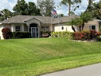 Charming home featuring a well-manicured lawn, lush landscaping, and decorative touches like flags and bench at 2864 Traverse Ave, North Port, FL 34286