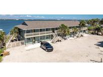 Two-story building featuring multiple units, surrounded by palm trees, water views and a car parked in the expansive parking area at 5041 N Beach Rd # 2A And 2B, Englewood, FL 34223
