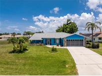 Charming blue home featuring a lush lawn, gray roof, stone accents, and well-maintained landscaping at 23 Bunker Cir, Rotonda West, FL 33947
