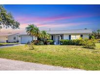 Charming single-story home with well-maintained lawn, lush landscaping, and a driveway leading to an attached garage at 305 E Wentworth Cir, Englewood, FL 34223