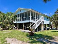 Inviting raised beach house with a screened porch and a well-maintained lawn under a bright blue sky at 9270 Little Gasparilla Is, Placida, FL 33946