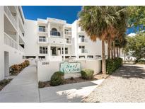 Surf Club Condo showcases a well-maintained white building with lush tropical landscaping and a welcoming entrance sign at 2380 N Beach Rd # 210, Englewood, FL 34223