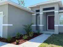 Beautifully landscaped gray home with a concrete walkway and a red front door at 311 Yule St, Port Charlotte, FL 33953
