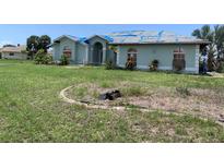 Exterior view of a single-story home needing repairs, with a neglected lawn and blue tarp on the roof at 1 Clubhouse Rd, Rotonda West, FL 33947