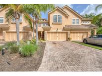 Inviting townhome exterior featuring a multi-car garage, brick driveway, and tropical landscaping including palms at 8228 Villa Grande Ct, Sarasota, FL 34243