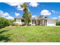 Charming single-story home featuring lush green lawn and mature tropical landscaping under a sunny blue sky at 7059 Quigley St, Englewood, FL 34224