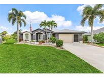 Charming single-story home with a lush green lawn, palm trees, and a welcoming driveway leading to an attached garage at 7130 Scarlet Sage Ct, Punta Gorda, FL 33955