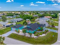 Aerial view of a vibrant turquoise home featuring a well-maintained lawn and lush landscaping at 9457 Heartwellville Ave, Englewood, FL 34224