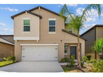 Beige two-story home featuring a two-car garage, and tropical landscaping with a palm tree at 2139 Stellar Brilliance Way, Lutz, FL 33558