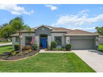Charming single-story home with a manicured lawn, lush landscaping, and a vibrant blue front door at 13365 Chesapeake Pl, Spring Hill, FL 34609