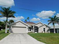 Well-maintained single-story home with lush lawn, mature trees, and a driveway leading to an attached two-car garage at 401 Malpelo Ave, Punta Gorda, FL 33983