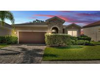 Charming single-story home with stone accents, a well-manicured lawn, and a brick paved driveway at 11825 Frost Aster Dr, Riverview, FL 33579