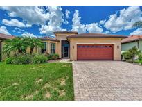 Tan house with red garage door, lush landscaping, and paved driveway at 20193 Pezzana Dr, Venice, FL 34292