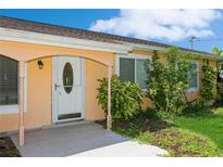 Quaint light orange home with white door and lush landscaping at 18069 Ohara Dr, Port Charlotte, FL 33948