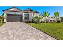 Modern home with dark garage door, paver driveway, and landscaping at 15060 Aquarius Cir, Port Charlotte, FL 33981