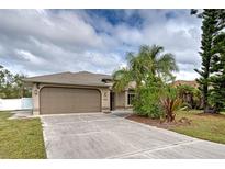 Tan house with attached garage, landscaping, and palm trees at 23102 Madelyn Ave, Port Charlotte, FL 33954
