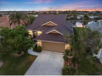 A beautiful home with a brown tile roof is surrounded by trees and overlooks a serene lake at sunset at 1307 Highland Greens Dr, Venice, FL 34285