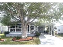 Gray mobile home with covered carport, landscaping, and mature tree at 727 Blackburn Blvd, North Port, FL 34287