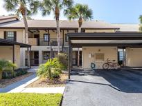 Condo building featuring a carport, palm trees, and lush landscaping in a well-maintained community at 380 Three Lakes Ln # F, Venice, FL 34285