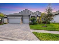 Beautiful home featuring a three-car garage, gray facade, well-kept lawn and a paver driveway and sidewalk at 19807 Bridgetown Loop, Venice, FL 34293