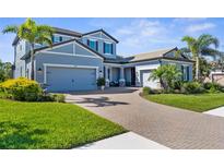 Beautiful two-story blue home with a three-car garage, brick driveway, and lush tropical landscaping at 19836 Bridgetown Loop, Venice, FL 34293