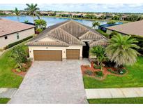 Aerial view of a house with a brick driveway, a three-car garage, and a beautiful lake view at 13238 Famiglia Dr, Venice, FL 34293