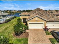 Lovely exterior of a home that features a tile roof, brick driveway, and a lush green lawn with landscaping and a lake view at 11644 Okaloosa Dr, Venice, FL 34293