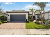 Charming single-story home with a tile roof, brick driveway, well-kept lawn, and tropical landscaping at 13867 Vadini St, Venice, FL 34293