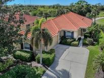Charming single-story home featuring a terracotta tile roof, lush landscaping, and a concrete driveway at 174 Treviso Ct, North Venice, FL 34275