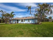 Charming light blue home featuring a lush lawn and tropical landscaping with palm trees against a blue sky at 8170 Casa De Meadows Dr, Englewood, FL 34224