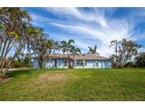 Single story home with light blue paint, palm trees, green grass, blue skies, and a grassy lawn at 8170 Casa De Meadows Dr, Englewood, FL 34224