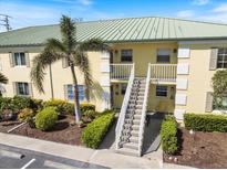 Yellow two-story condo building with a green roof, lush landscaping, and an exterior staircase leading to the second floor at 944 Capri Isles Blvd # 103, Venice, FL 34292