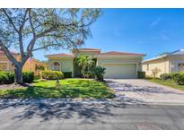 Charming single-story home with a well-manicured lawn and brick driveway under a clear sky at 108 Corte Del Asolo, Venice, FL 34285