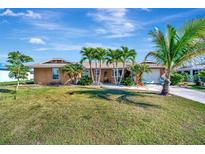 Charming single-story home with a well-manicured lawn, palm trees, and a welcoming facade under a sunny sky at 13534 Alberta Ave, Port Charlotte, FL 33981